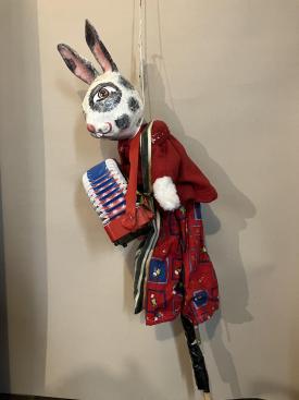 Lapin vêtu d'un pantalon rouge à motifs et d'une veste rouge, avec un accordéon