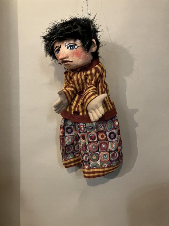 Tibougon ronchon, jeune garçon aux cheveux noirs, vêtu d'un pantalon bariolé et d'une veste à rayures jaunes et brunes