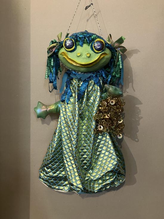 Grenouille verte vêtue d'une robe à écailles et portant un sac à main doré