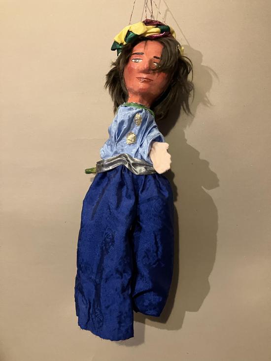 Jeune homme à longs cheveux bruns, vêtu d'un pantalon bleu roi et d'une chemise bleu clair