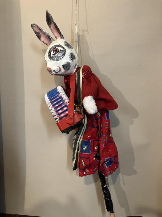 Lapin vêtu d'un pantalon rouge à motifs et d'une veste rouge, avec un accordéon