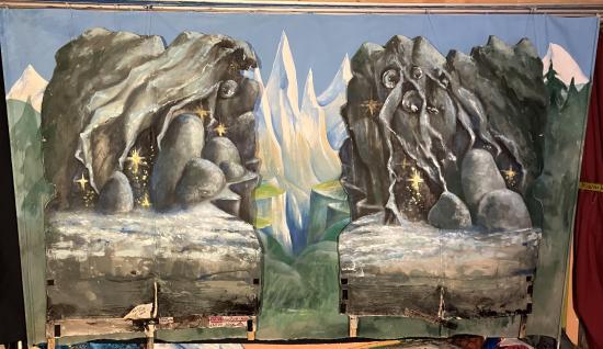 Forêt de sapins, montagnes enneigées, précipice et deux rochers au premier plan